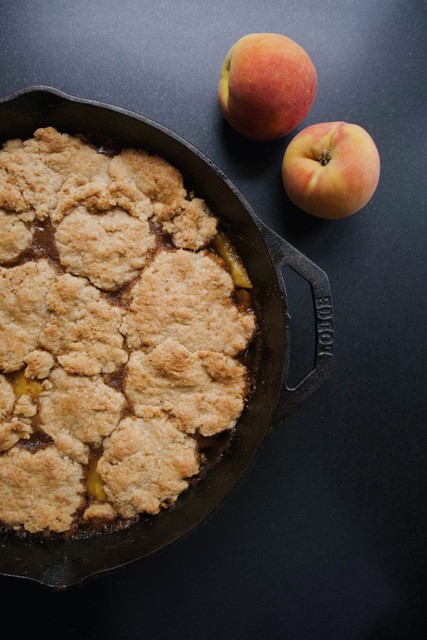 peach cobbler in skillet next to peaches